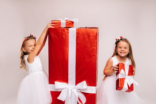 Dos niñas con regalos de Navidad sobre un fondo blanco y un gran regalo