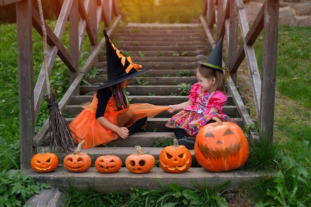 Dos niñas sentadas en una antigua escalera de madera con calabazas talladas de Halloween