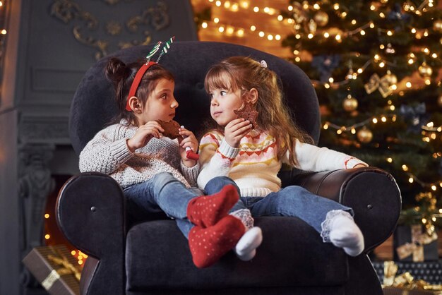 Dos niñas sentadas y comiendo galletas en una habitación decorada con Navidad.