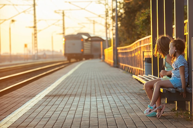 dos niñas se sientan en el banco de la estación por la noche y miran el tren que sale