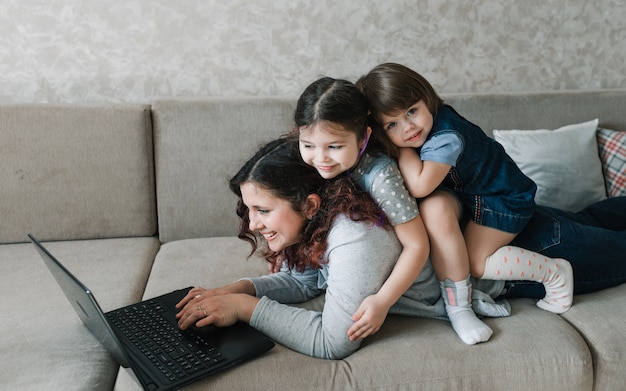 Dos niñas se sientan en la espalda de su madre mientras trabajan en la computadora. trabajo remoto en casa