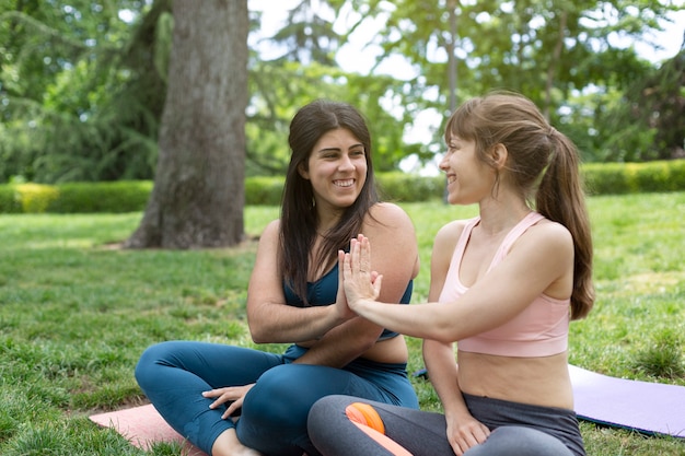 Dos niñas sonrientes en ropa deportiva chocan los cinco. Están en el parque sentados en el césped. Espacio para texto.