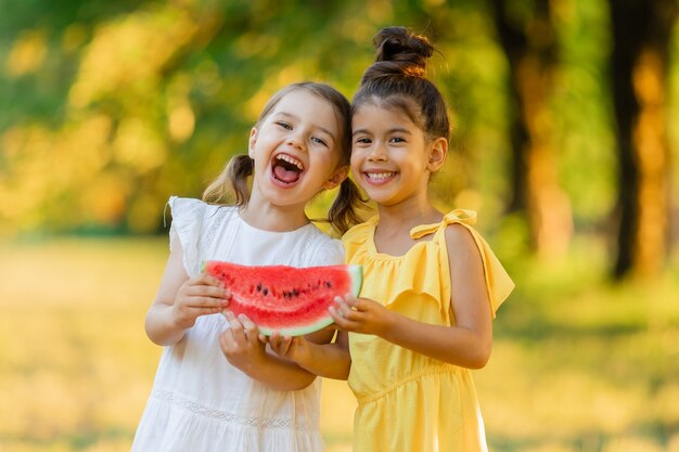 Dos niñas sonrientes sostienen una rodaja de sandía en sus manos.Los niños comen fruta al aire libre