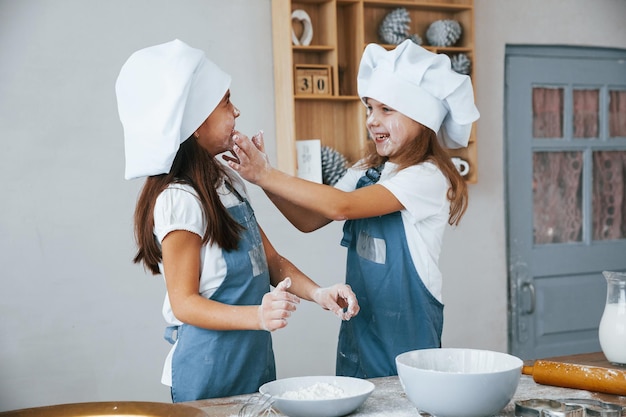 Dos niñas con uniforme de chef azul se divierten con harina en la cocina