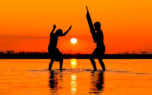 Foto dos niño jugando can, estilos musicales del noreste de tailandia en el lago en el fondo del atardecer.