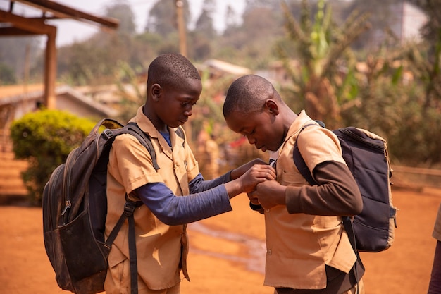 Dos niños africanos con sus mochilas pesadas juegan en el patio de la escuela