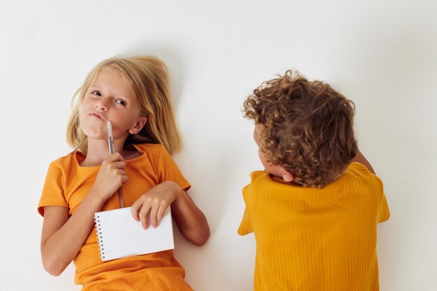 Dos niños alegres dibujando juegos divertidos con el estilo de vida infantil del bloc de notas inalterado