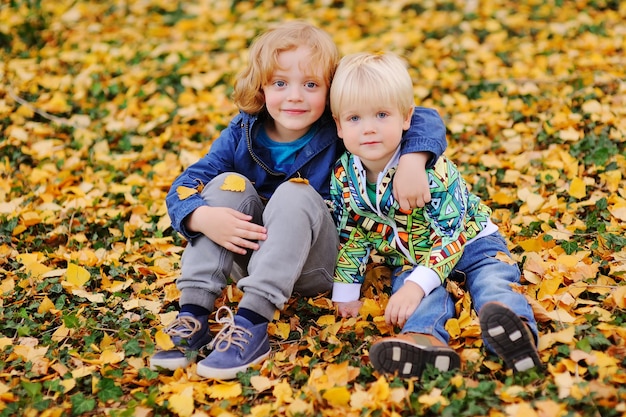 Dos niños - amiguitos abrazándose contra las hojas de otoño en el parque.
