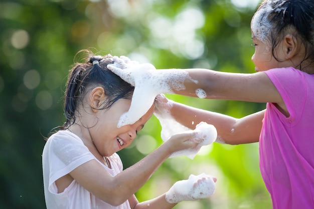 Dos niños asiáticos felices chica que se divierten para baño y jugar con espuma juntos en el exterior