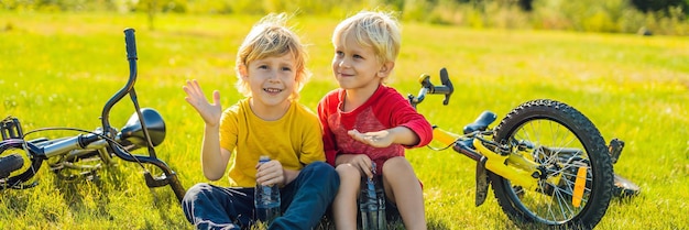 Dos niños beben agua en el parque después de andar en bicicleta en formato largo