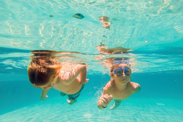 Dos niños buceando con máscaras bajo el agua en la piscina.