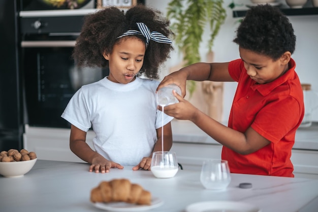 Dos niños en la cocina con vasos de leche en las manos.