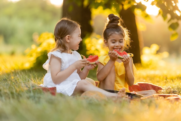 Dos niños comiendo sandía en el jardín Los niños comen frutas al aire libre Refrigerio saludable para los niños