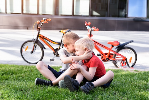 Dos niños se comunican sentados en el césped. Descanse después de andar en bicicleta, bicicletas