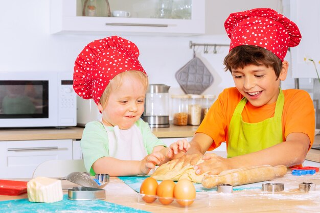 Foto dos niños desmoronan la masa con las manos en sombreros de chef