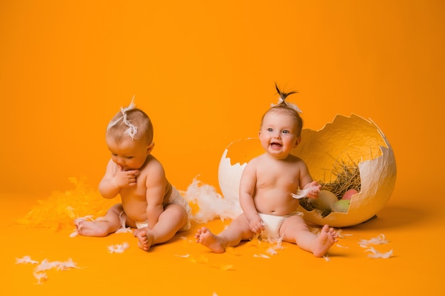 Dos niños en un disfraz de pollo con huevos en un amarillo, Pascua