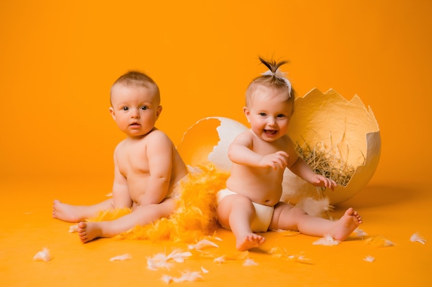 Dos niños en un disfraz de pollo con huevos en una pared naranja, concepto de Pascua