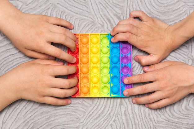 Dos niños empujan popit sensorial al mismo tiempo sobre fondo gris. Juguete pop-it antiestrés. Inquietud sensorial de silicona arco iris. Nuevo juguete de silicona de moda popular.