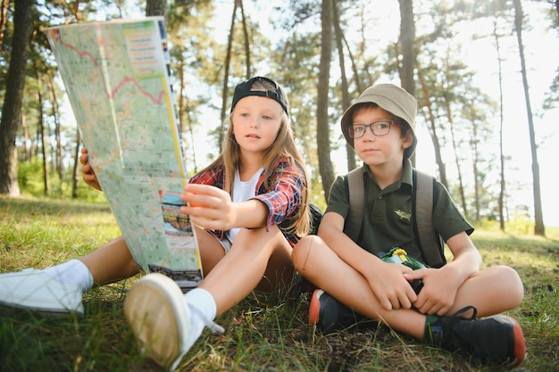 Dos niños felices divirtiéndose durante la caminata por el bosque en un hermoso día en el bosque de pinos Lindo boy scout con binoculares durante la caminata en el bosque de verano Conceptos de exploración de aventura y turismo de senderismo