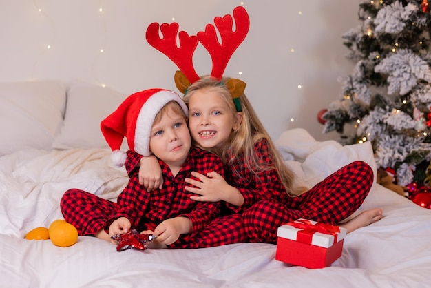 dos niños felices en pijama para Navidad clasifican regalos y juegan con juguetes navideños