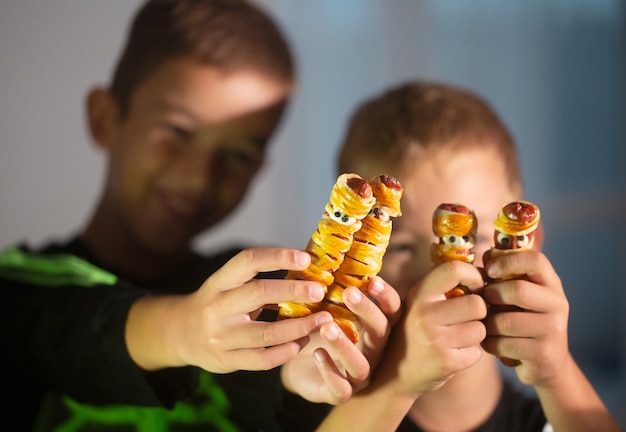 Dos niños felices sosteniendo bocadillos de Halloween en forma de momia hechos de salchicha