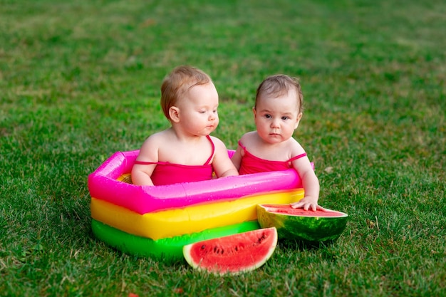 Dos niños de gemelos alegres nadan en una piscina inflable en verano en la hierba verde con un espacio de sandía para texto