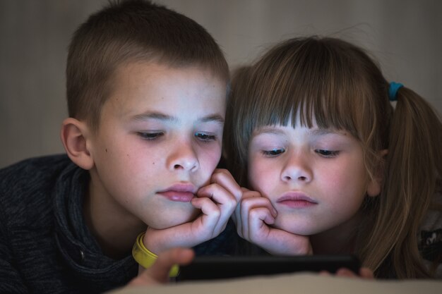 Dos niños hermano y hermana viendo video en la pantalla del teléfono inteligente juntos.