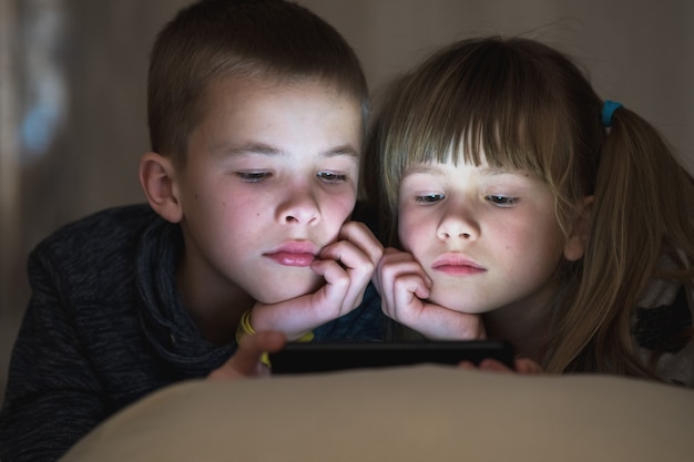Dos niños hermano y hermana viendo video en la pantalla del teléfono juntos.