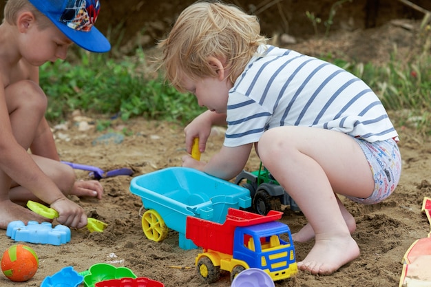 Dos niños juegan en la arena con juguetes de plástico.