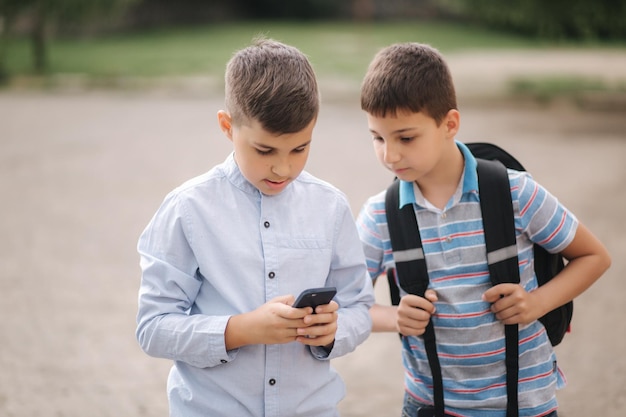 Dos niños juegan juegos en línea después de las clases escolares Los niños jóvenes sonríen y usan el teléfono