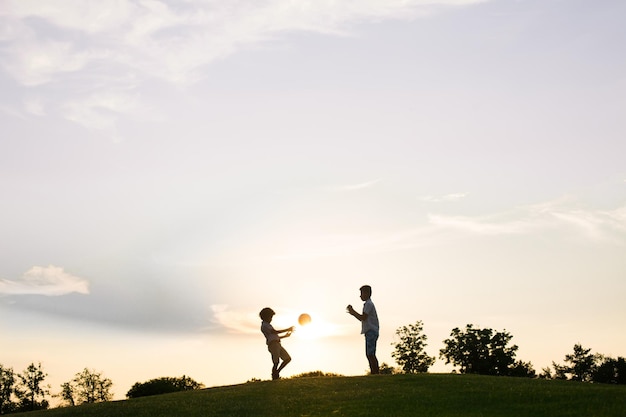 Dos niños juegan con una pelota al atardecer.