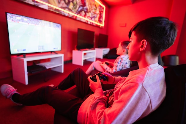 Dos niños jugadores juegan a la consola de videojuegos gamepad de fútbol en la sala de juegos roja