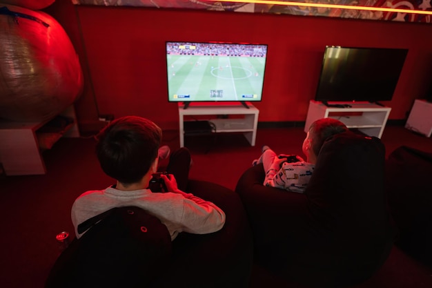 Dos niños jugadores juegan a la consola de videojuegos gamepad de fútbol en la sala de juegos roja