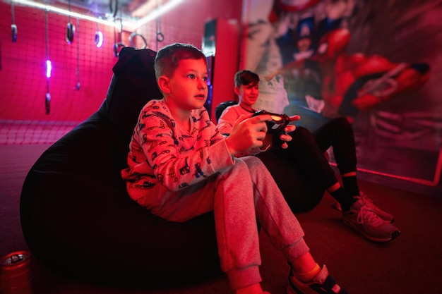 Dos niños jugadores juegan a la consola de videojuegos gamepad en la sala de juegos roja