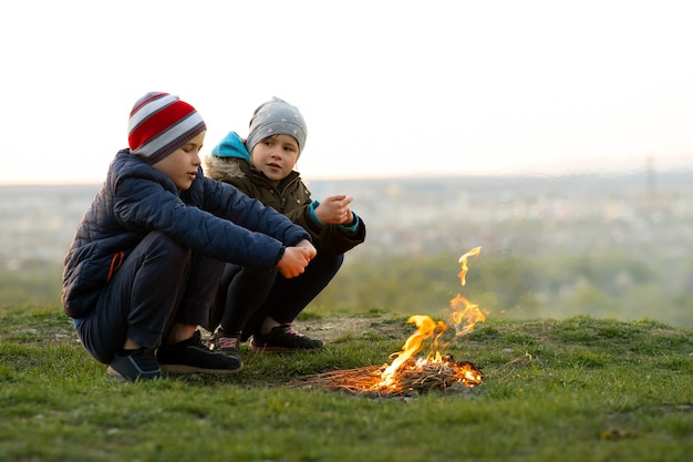 Dos niños jugando con fuego al aire libre cuando hace frío.