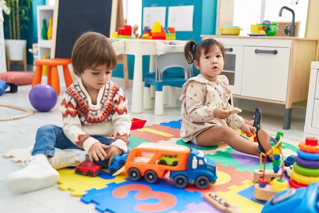 Dos niños jugando con juguetes de coches sentados en el suelo en el jardín de infantes