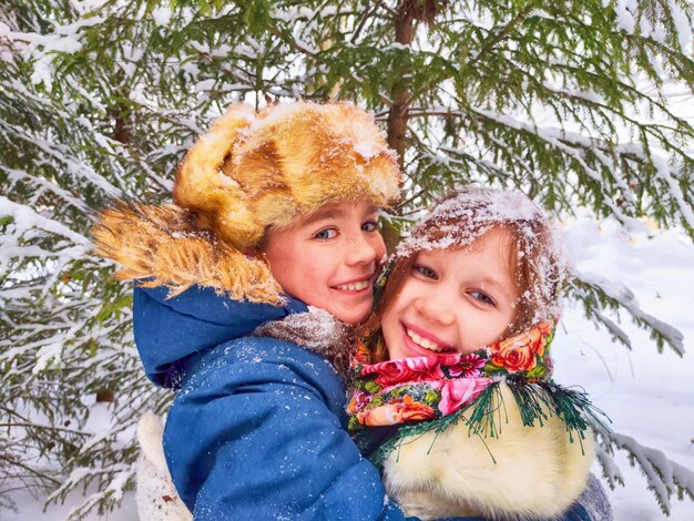 Dos niños lindos y alegres en el bosque de nieve de invierno se toman fotos con ropa estilizada de