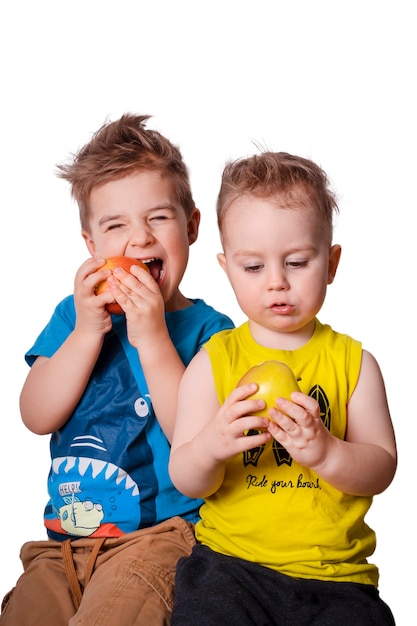 Dos niños lindos en el fondo blanco, comiendo manzanas. Imagen aislada.