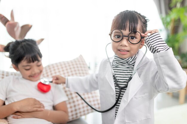 Dos niños lindos juegan a médico y hospital usando estetoscopio Amigas chicas divirtiéndose en casa o en el preescolar