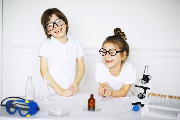 Dos niños lindos en la lección de química haciendo experimentos aislados sobre fondo blanco.