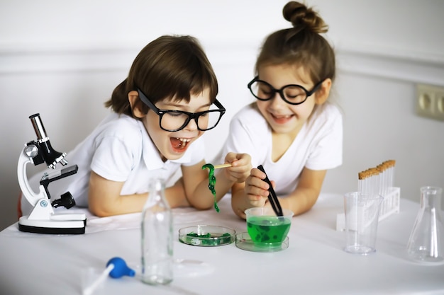 Dos niños lindos en la lección de química haciendo experimentos aislados sobre fondo blanco.
