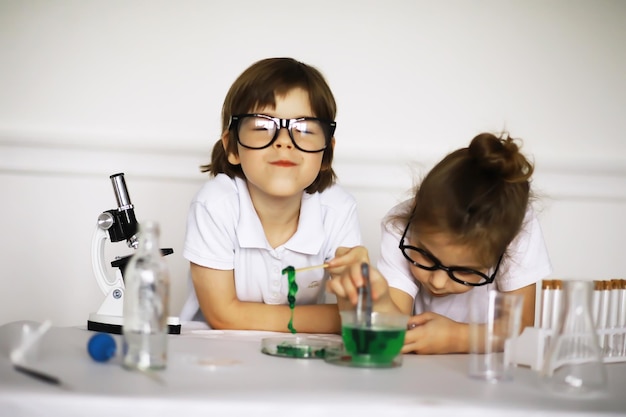 Foto dos niños lindos en la lección de química haciendo experimentos sobre fondo blanco.