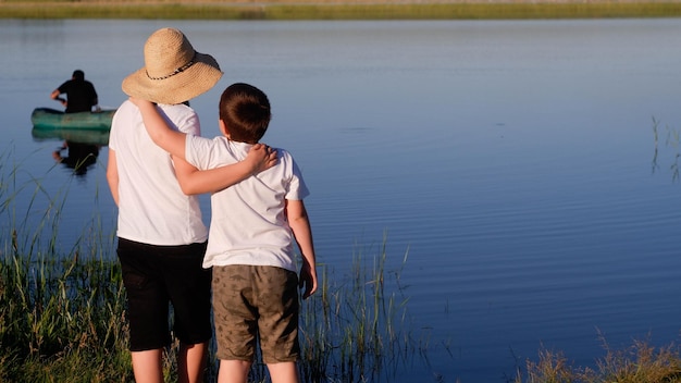 Dos niños miran al hombre en un tablero en el lago.