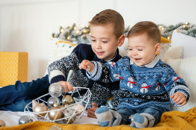 Foto dos niños muchacho caucásico jugando con adornos navideños y riendo en la cama. tarjeta de navidad maravillosa con niños felices. los niños se divierten y disfrutan de las vacaciones de año nuevo y navidad.