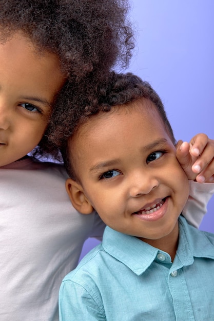 Dos niños negros felices posando en la cámara y sonriendo alegremente sobre púrpura