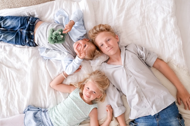 Dos niños y niñas rubios están acostados juntos en la cama, mirando y sonriendo.