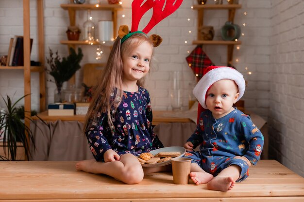 Dos niños, un niño y una niña, comen galletas en la cocina el día de Navidad.
