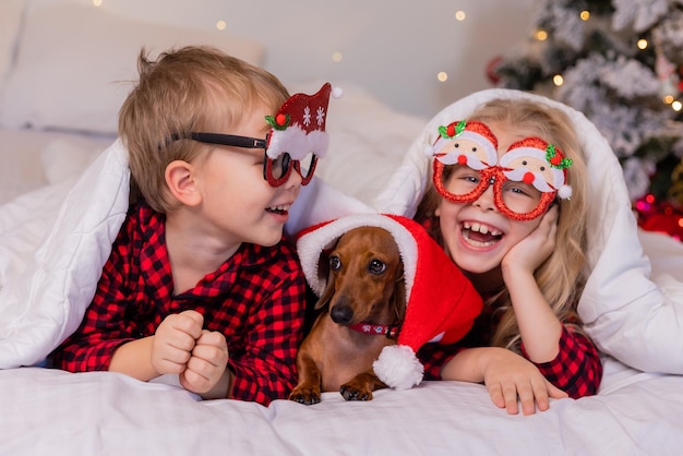 dos niños, un niño y una niña, están acostados en la cama con su querida mascota para Navidad
