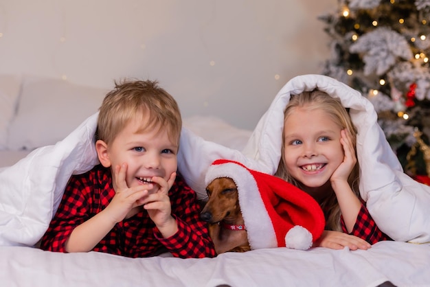 dos niños, un niño y una niña, están acostados en la cama con su querida mascota para Navidad