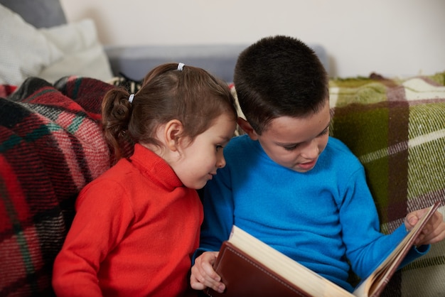 Dos niños, un niño y una niña sentados juntos mirando un álbum de fotos familiar. Hermano y hermana